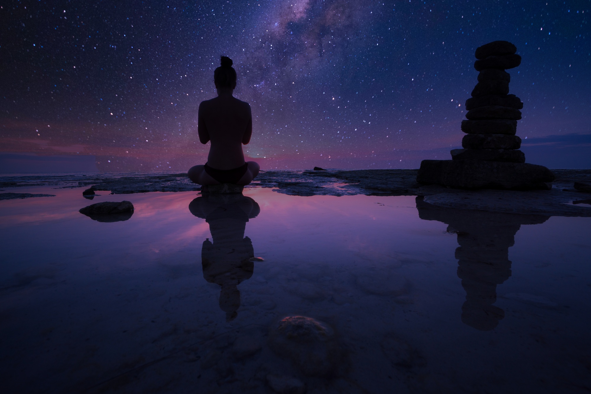 Wallpaper of a girl doing meditation at night at the seashore under the blue-purple starry sky